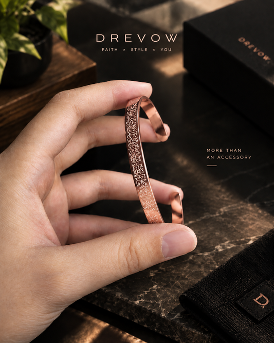 A hand holds a rose gold bangle bracelet with a textured, openwork pattern. Ayatul Kursi Bracelet - Rose Gold Color
